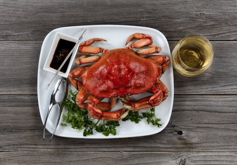 Whole cooked Dungeness crab in dinner table setting with wine