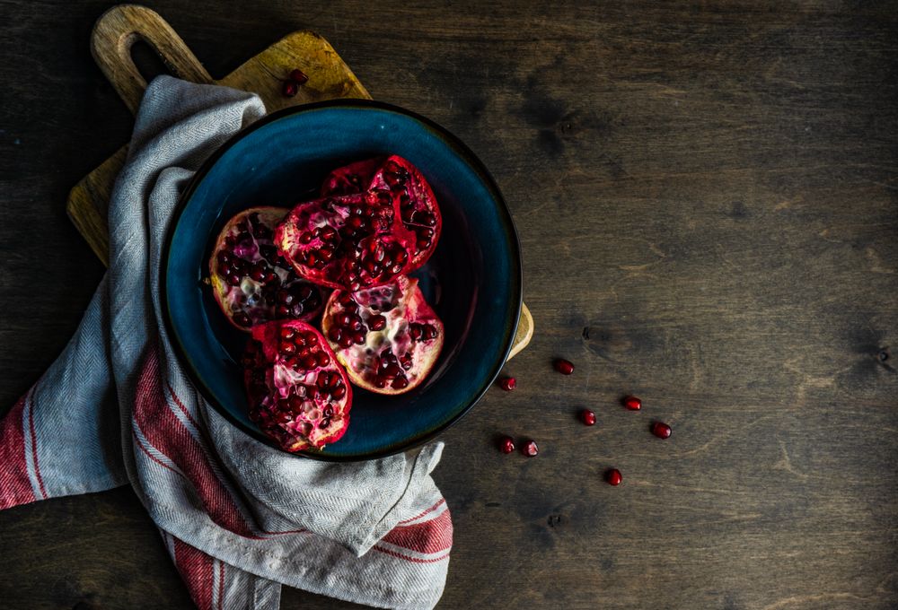 Top view of ceramic bowl of open pomegranates on wooden table
