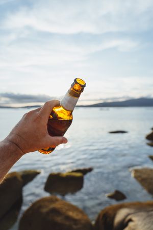 Bottle of beer in hand with seascape on background