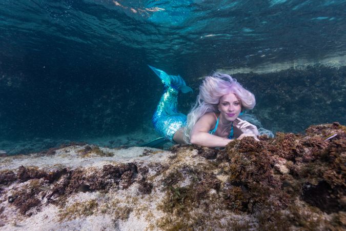 Blond fairytale female mermaid exploring underwater