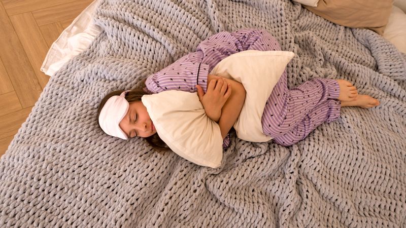 Teenage girl holding pillow, lying in bed.