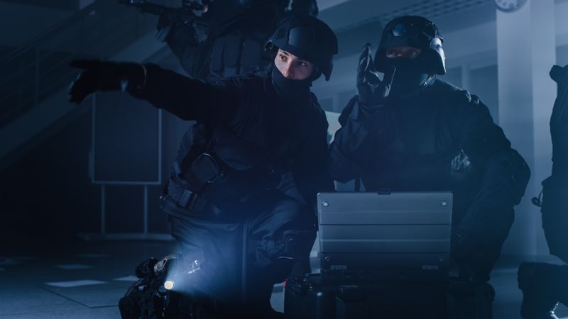 Masked Team of Armed SWAT Police Officers with Rifles are in Dark Seized Office Building with Desks and Computers.