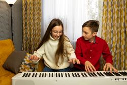 Teenagers boy and girl smiling while playing digital piano