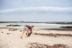 Content modern woman picking litter from sandy seashore