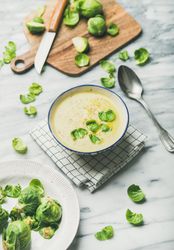 Brussels sprout soup, garnished with fresh sprouts, next to wooden board, vertical composition