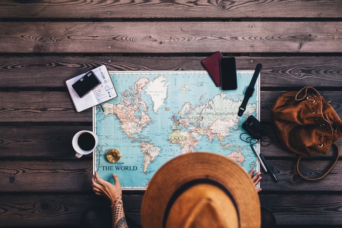 Young woman planning a vacation using world map and compass along with other travel accessories
