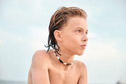 Shirtless boy wearing shell necklace looking away at beach