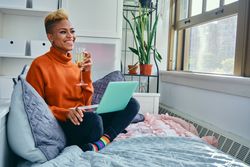 Happy Black woman laughing at a laptop with champagne flute in a bright modern home