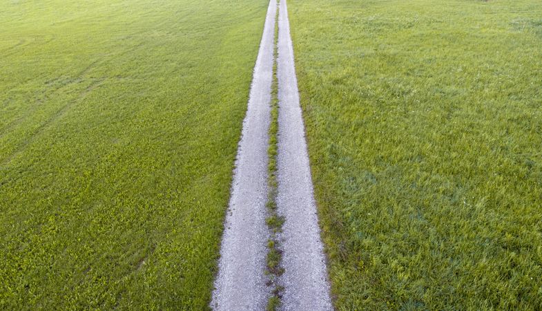 Green grass meadow aerial view with a countryside road passing through
