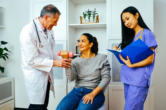 Smiling doctor and physiotherapist working with patient during arm rehab exercises