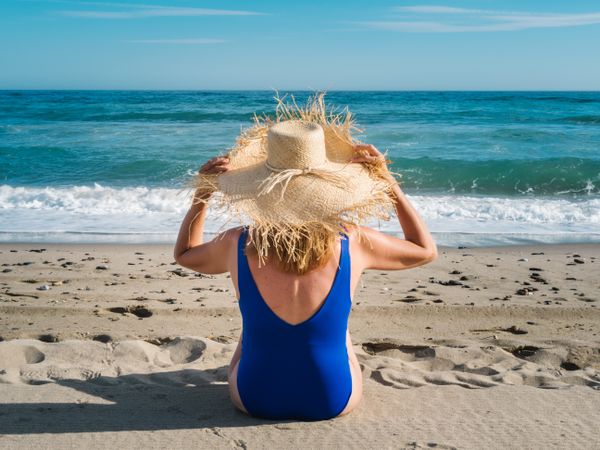Woman in blue swimsuit and hat on sandy beach