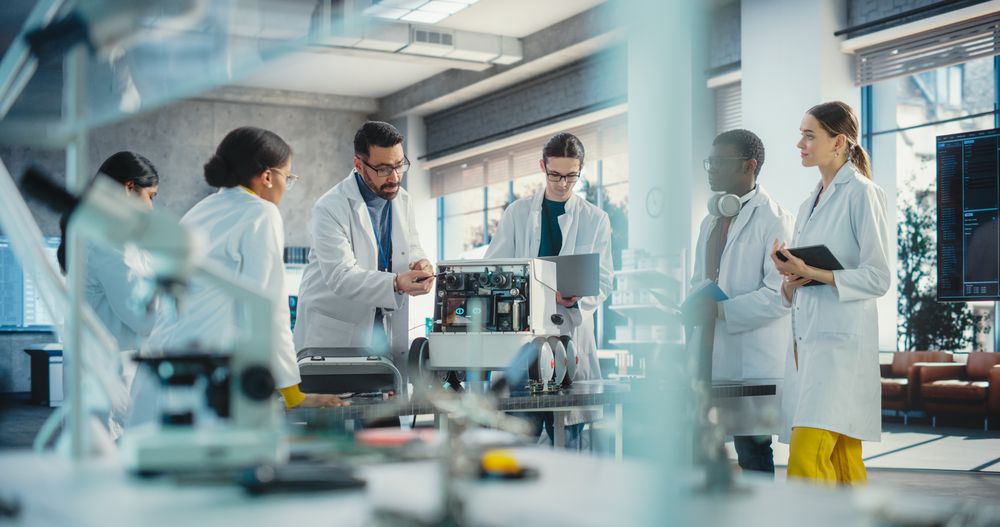 Diverse Team of Industrial Robotics Specialists Gathered Around a Table With a Mobile Robot.