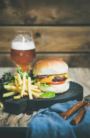 Classic hamburger with fries and beer at wooden restaurant table