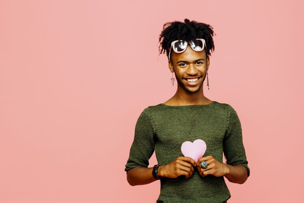 Portrait of a smiling young man holding a pink heart, isolated on pink studio background