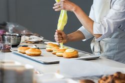 Crop cook decorating Berliners with cream in kitchen