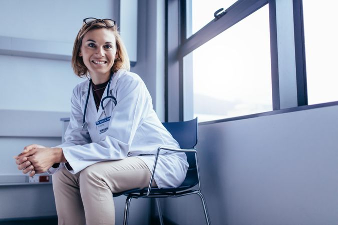 Portrait of smiling female doctor sitting on chair in hospital room