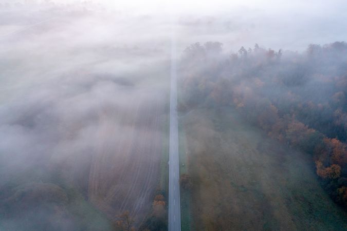 Drone image with a straight road crossing an autumn forest on a cold morning in October