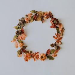 Wreath made of autumn fruits and leaves on light background