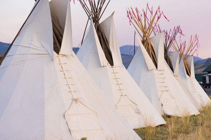 Montana, United States - August 17, 2022: Line of teepee in front of Rocky Mountains at dusk