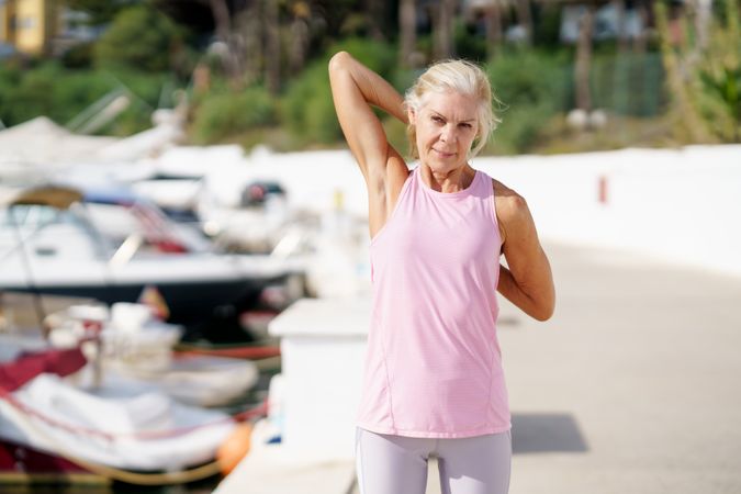 Older woman in pink sports wear stretching her arms after workout