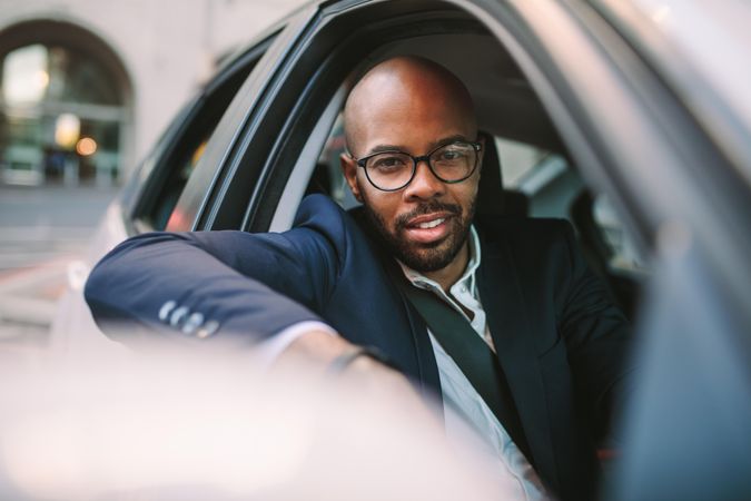 Businessman in suit peeking out of car window and looking at camera while driving