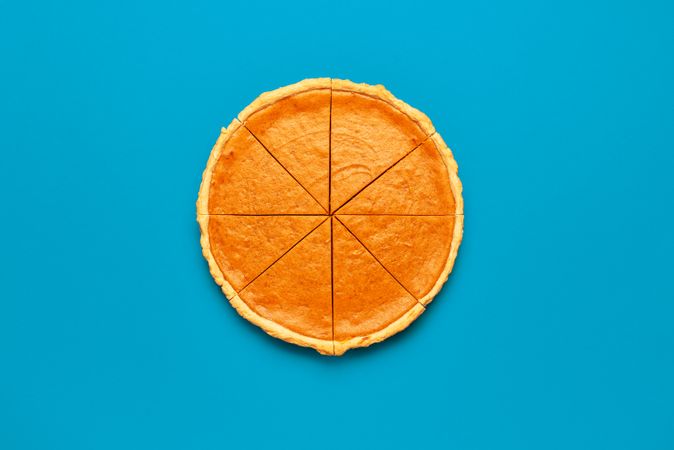 Sliced pumpkin pie, top view on a blue table