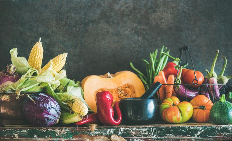 Fresh produce on counter with dark background with halved squash, corn, cabbage, with copy space