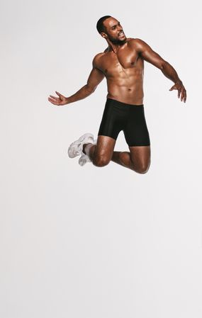 Male athlete jumping in mid air against light background