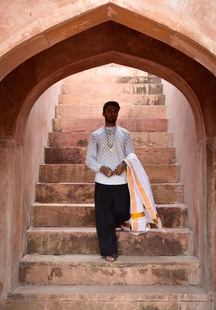 Man in light traditional outfit  standing on brown concrete stairs