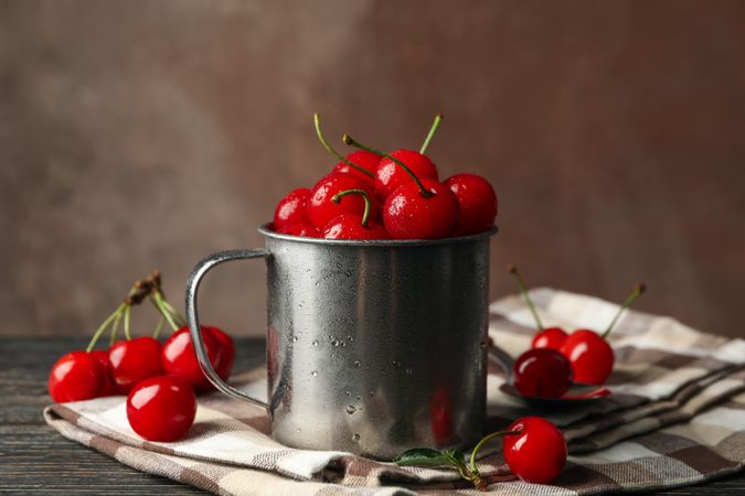 Towel and metal mug with cherry on wooden background. Summer plant