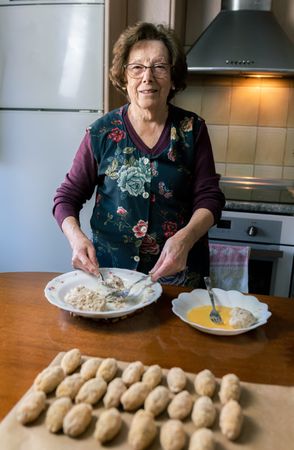 Happy grandmother preparing lots of croquettes at home