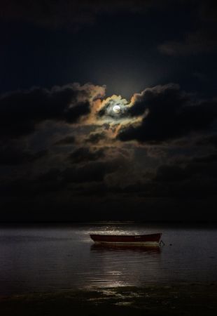 Full moon on cloud night above an ocean with a boat