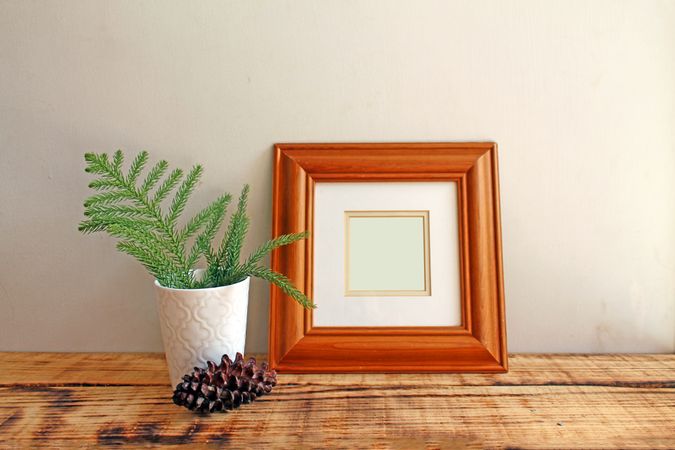 Square wooden picture frame on wooden desk with branch and pinecone mockup