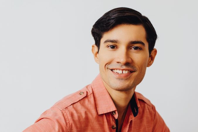 Headshot of smiling Hispanic male looking at camera in grey studio, copy space