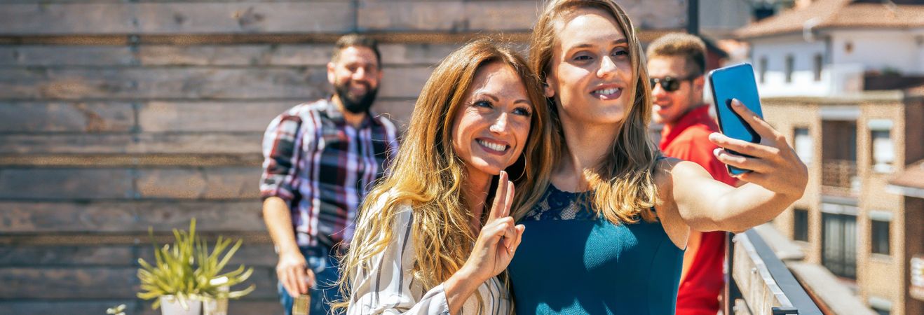Two female friends taking a selfie in rooftop on a summer party