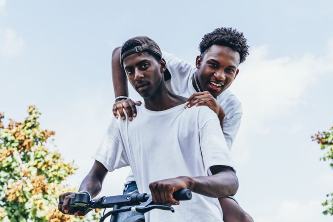 Black man riding on electric scooter in park with friend on back