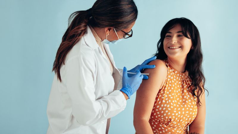 Mature female doctor giving injection to woman on blue background