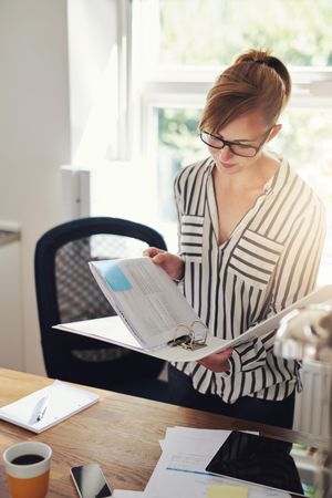Female in striped shirt looking through binder in her home office, vertical