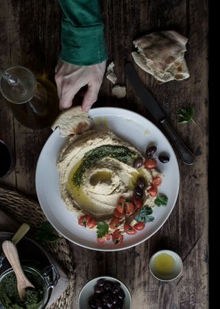 Crop hand dipping flatbread into hummus pesto with tomatoes and beans