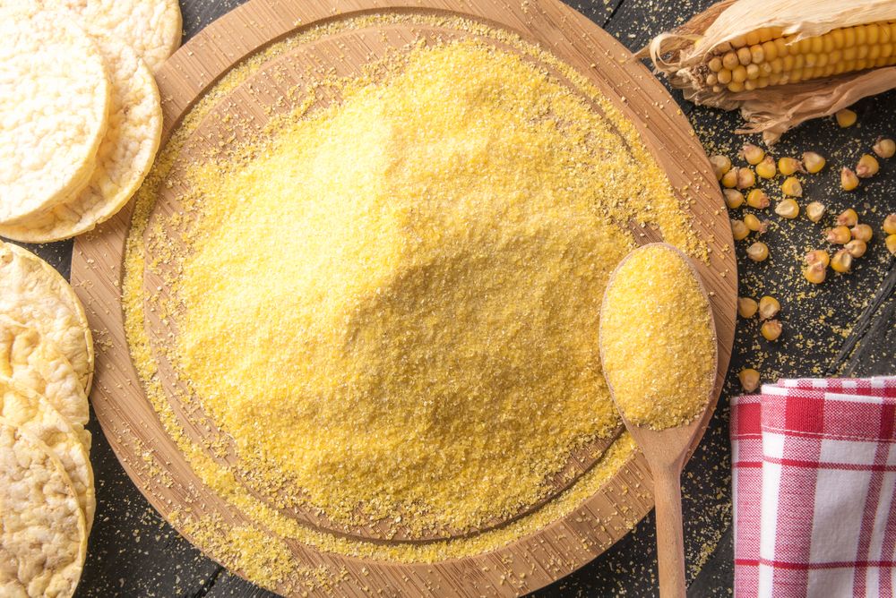Top view of pile of corn flour on  round wooden board surrounded by corn, grains and tortillas
