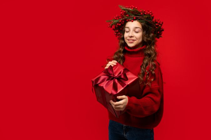Teen girl wearing Christmas berry wreath holding red gift box.