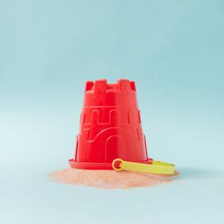 Upside down sand castle bucket with spilled sand against pastel blue background