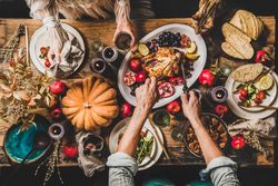 Autumnal table with squash and candles with man carving roast chicken and woman holding wine glass