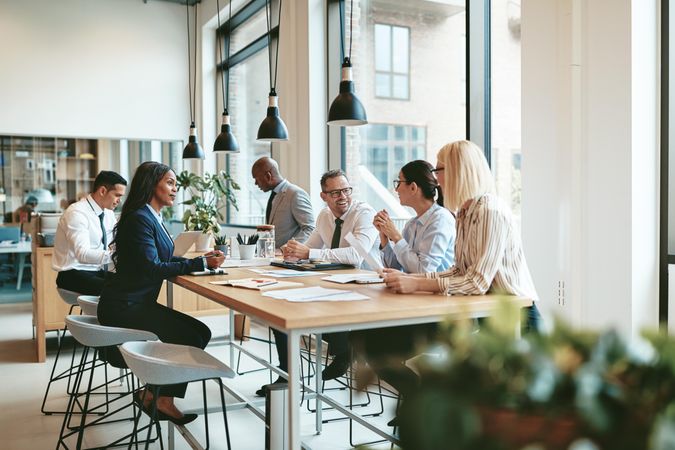 Group of people smiling while discussing work at a long table in a bright office