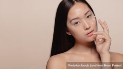 Close up of a beautiful young woman applying cream to her face 0W8215