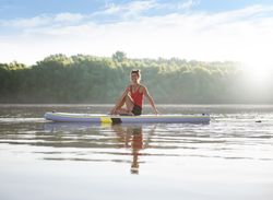 Woman smiling on paddleboard on fresh lake in the morning surrounded by trees