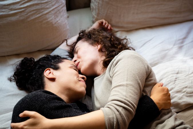 Two women lying down on bed in intimate embrace closing their eyes