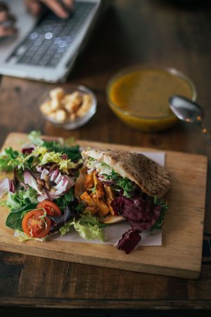 Chicken pita sandwich on a wooden table with laptop in background