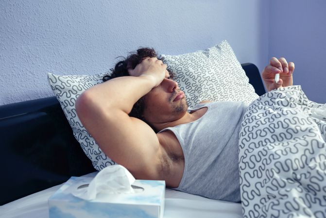 Sick man with tissues checking temperature in bed