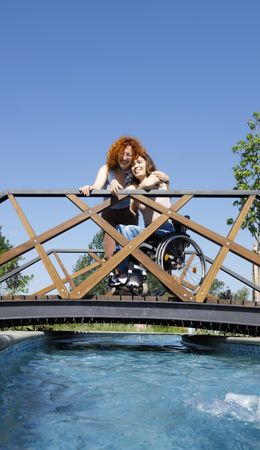 Woman in a wheelchair and female friend on bridge above water